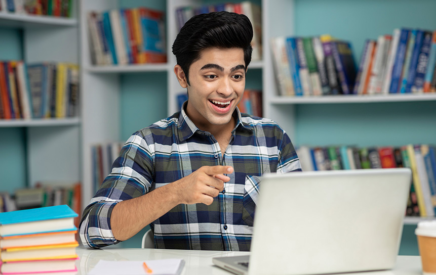 Male student excitedly smiling at the laptop and taking lectures.