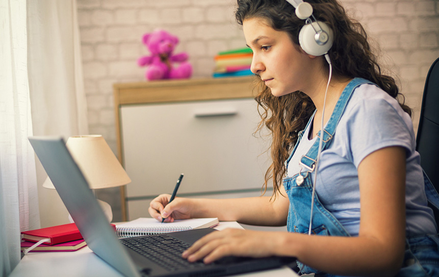 A teenage girl with headphones using a laptop to finish her homework.